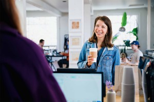 Photo-Woman holding coffee cup in front of a cashier
