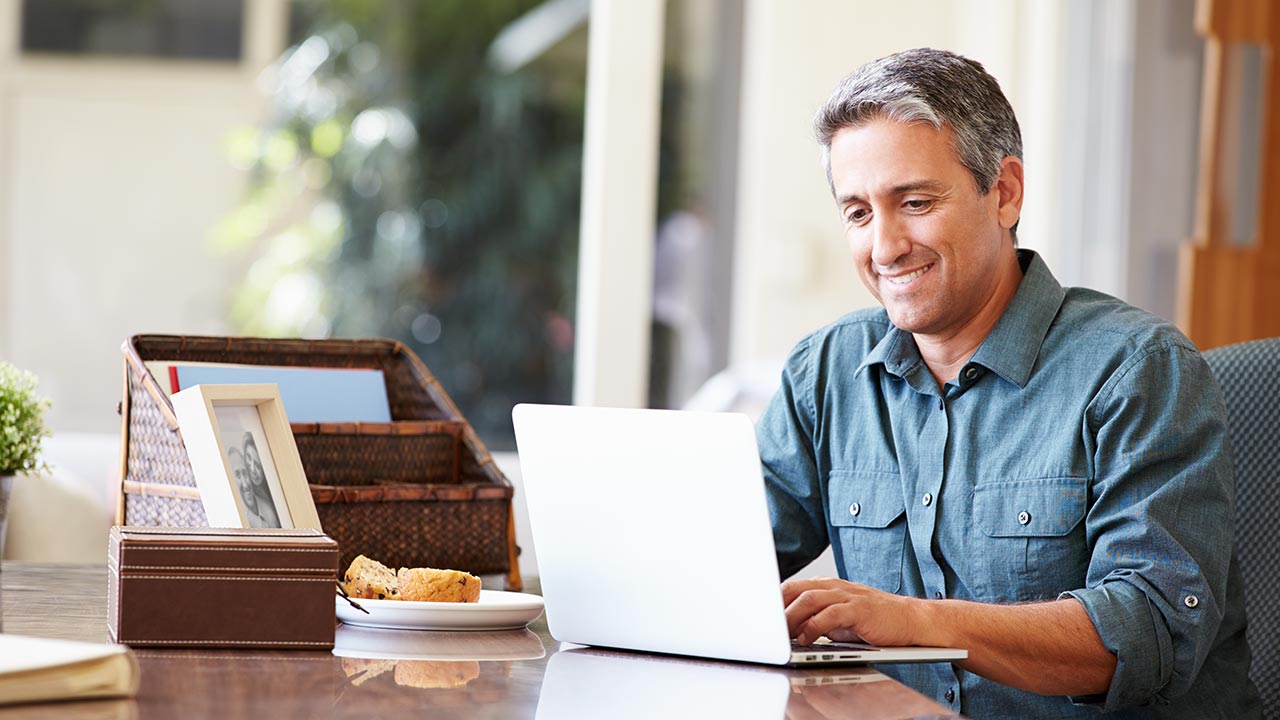 Middle-age man at kitchen table viewing laptop